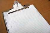 A clipboard on the desk with a piece of ruled paper attached