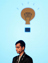 A person with a mic near his mouth stands with a lightbulb image above his head