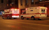 Two ambulances with lights flashing follow one another down the street