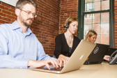 Three workers sitting at a long table working on laptops