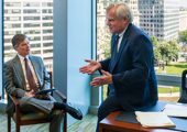 A CEO sits on the edge of a desk in an office having a discussion