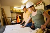 Two civil engineers stand over some plans on a short table