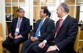 Three business people in suits sit in chairs beside each other talking