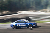 A sporty blue coupe races down a track with a blurred scenery behind it