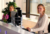 Two team members are turned toward the camera while behind their thin desk and monitors