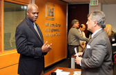 Two people in business suits talk while others have discussions in the background